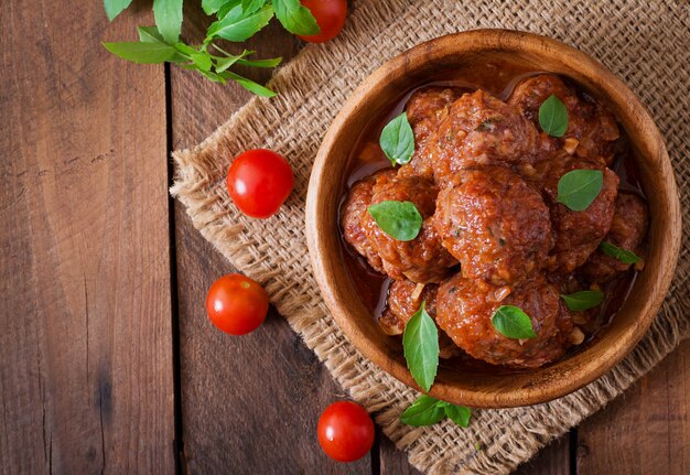 Meatballs in sweet and sour tomato sauce and basil in a wooden bowl