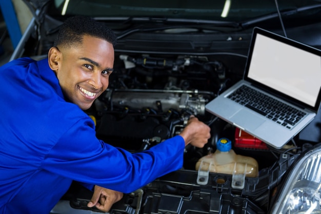 Mechanic examining car engine with help of laptop