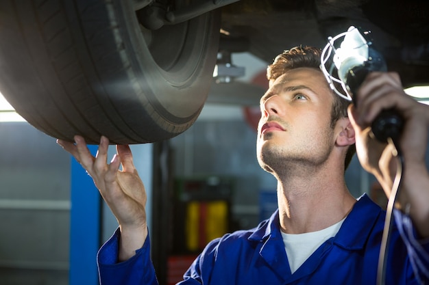 Mechanic examining car tyre using flashlight