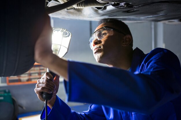 Mechanic examining car tyre using flashlight