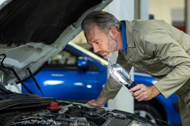Mechanic examining a car with lamp