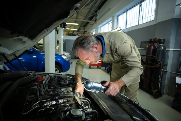 Mechanic examining a car with lamp