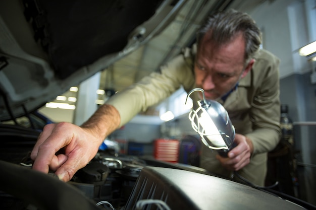 Mechanic examining a car with lamp