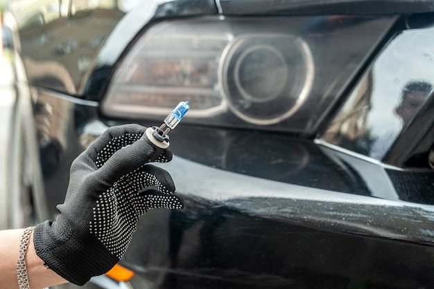 Mechanic hand holding halogen light bulb near on car headlight, repair