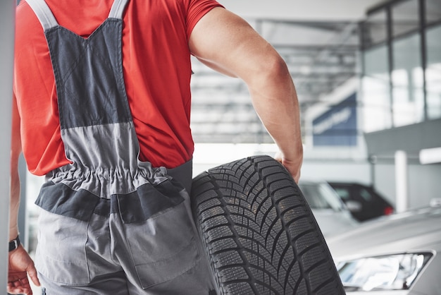 Meccanico in possesso di un pneumatico pneumatico presso il garage di riparazione. sostituzione di pneumatici invernali ed estivi.