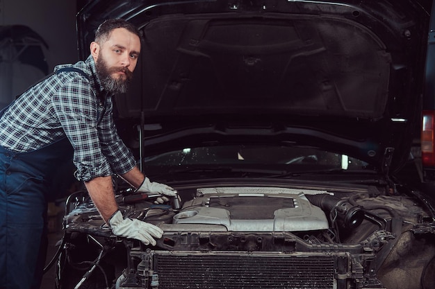 Mechanic man in uniform repairing car in the garage. Service station.