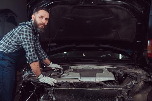 Mechanic man in uniform repairing car in the garage. Service station.