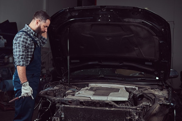 Mechanic man in uniform repairing car in the garage. Service station.