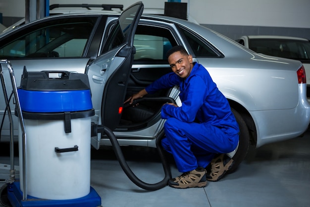 Mechanic servicing car with vacuum cleaner