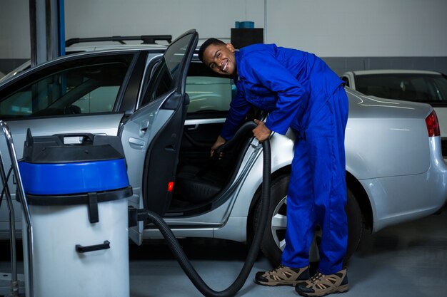 Mechanic servicing car with vacuum cleaner