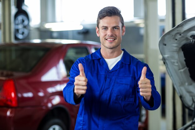 Mechanic standing in repair shop showing thumbs up