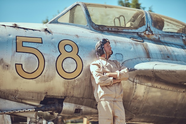 Mechanic in uniform and flying helmet standing near an old war fighter-interceptor in an open-air museum.