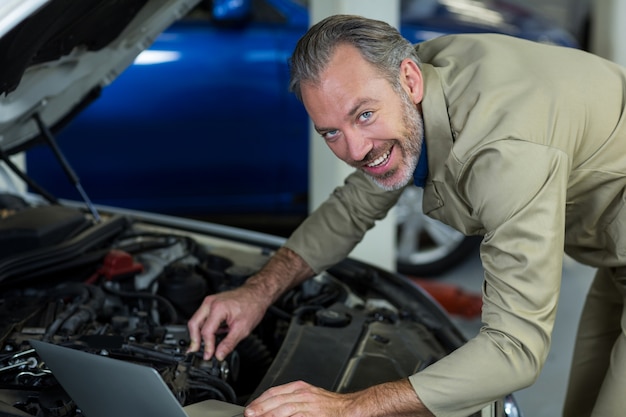 Mechanic using laptop while servicing car engine