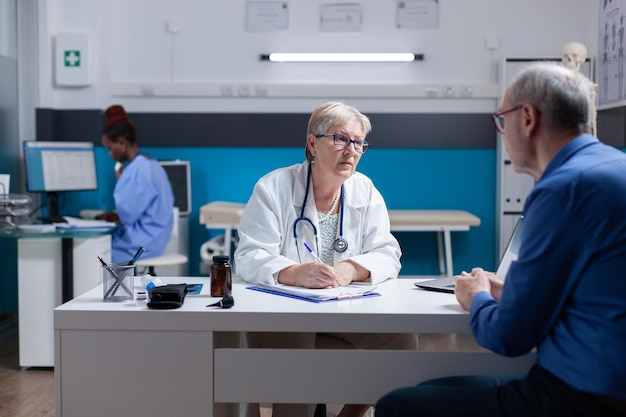 Medic doing signature on checkup papers to give prescription medicine to patient. Woman doctor signing documents after healthcare consultation, giving treatment to senior man with disease.