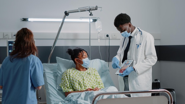 Free photo medic explaining cardiovascular figure on digital tablet to patient with sickness in bed. specialist holding cardiology image with heart organ on display, doing consultation during pandemic