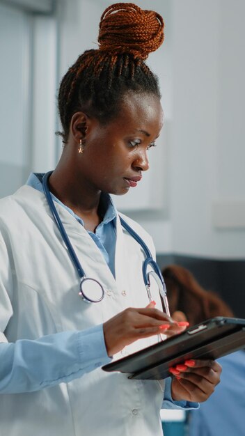 캐비닛의 의료 시스템용 태블릿 화면을 보고 있는 메딕. 의사 사무실에서 검진 방문 및 의료 치료를 위해 터치 스크린이 있는 디지털 장치를 사용하여 흰색 코트를 입은 의사.
