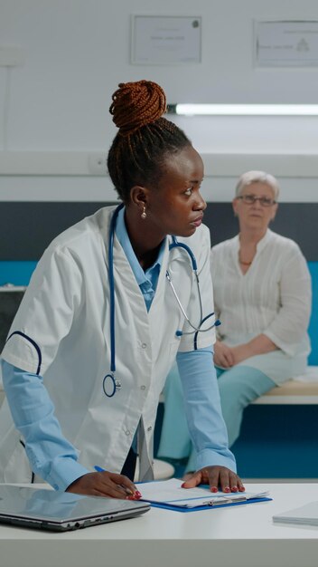 Medic and nurse talking about examination results while using patient document files on desk in cabinet at healthcare clinic. Doctor and medical assistant working on disease treatment