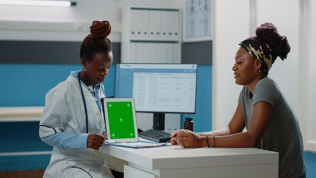 위생병은 녹색 화면이 있는 태블릿을 가리키고 상담을 위해 환자와 이야기합니다. 격리된 배경 및 모형 템플릿이 있는 크로마 키를 보고 있는 기술을 가진 의사와 여성