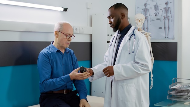 Free photo medic specialist holding bottle of pills to cure old patient with sickness, giving prescription medicine and antibiotics treatment to elderly man. doctor doing checkup consultation.