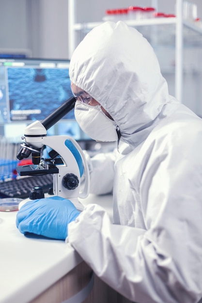 Free photo medic in time of global pandemic working on microscope dressed in ppe suit