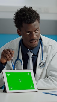 Medic using professional tablet with horizontal green screen display for senior patient healthcare. doctor with mockup template of chroma key isolated background on desk explaining device