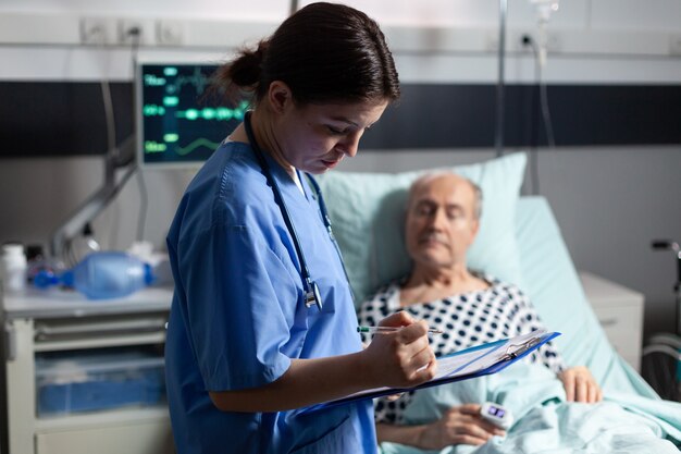 Medical assistant checking treatment of senior man reading notes on clipboard