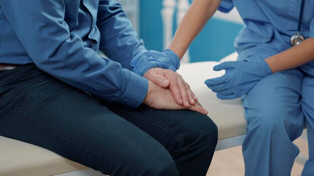 Medical assistant comforting senior patient to help with recovery, showing compassion after finding out health care diagnosis. Nurse giving support after sharing disease news. Close up.