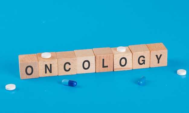 Medical concept with medical pills, oncology word on wooden cubes on blue table high angle view.