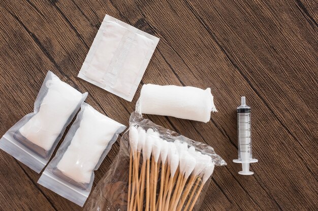 Medical cotton gauze bandage; syringe and pack of cotton swab on wooden table