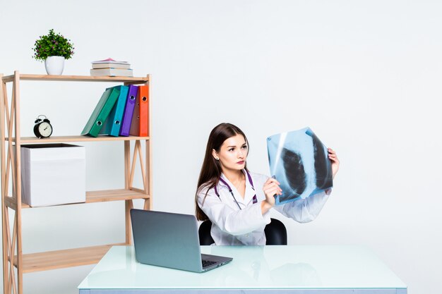 Medical doctor analysing x-ray image handheld, sitting at office desk.