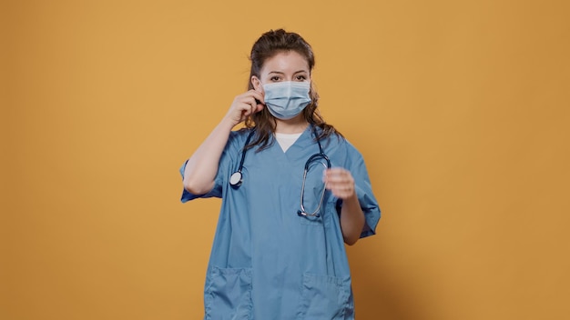 医療概念でサージカルマスクを取り外して腕を組んで自信を持ってポーズをとって立っている医師。スタジオで聴診器を身に着けている女性メディックの肖像画は、covid保護を脱いでいます。
