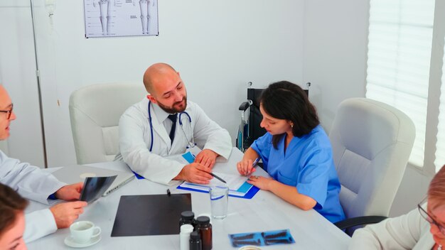 Medical expert talking with medical staff during healthcare meeting in hospital conference room explaining radiographys. Clinic therapist talking with colleagues about disease, medicine professional