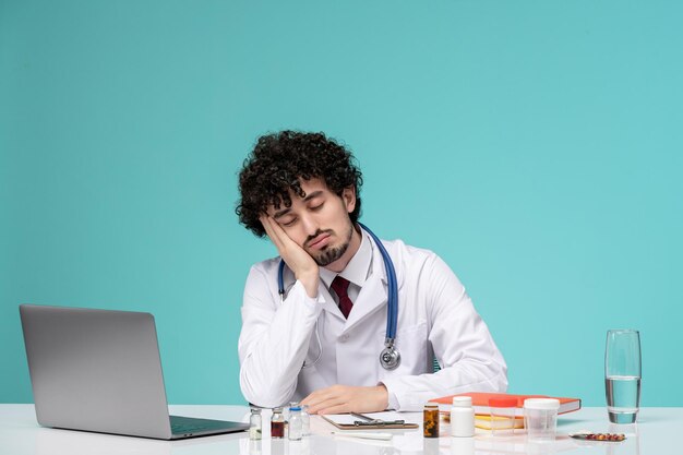 白衣を着た医療若い真面目なハンサムな医者がコンピューターに取り組んでいる疲れた睡眠