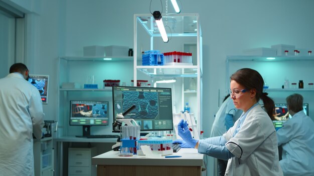 Medical lab worker analyzing blood serum conducting virus test in modern equipped lab late at night. Team of specialists examining vaccine evolution using high tech for treatment against covid19