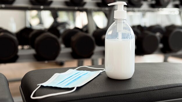 Medical mask and hand sanitizer on gym bench