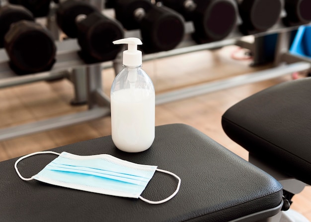 Medical mask and hand sanitizer on gym bench