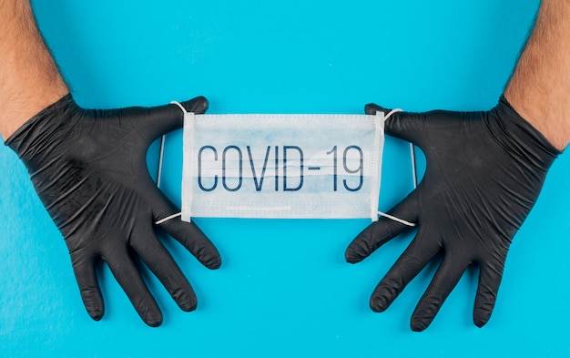 Medical mask with text covid-19 in a hands with black gloves top view