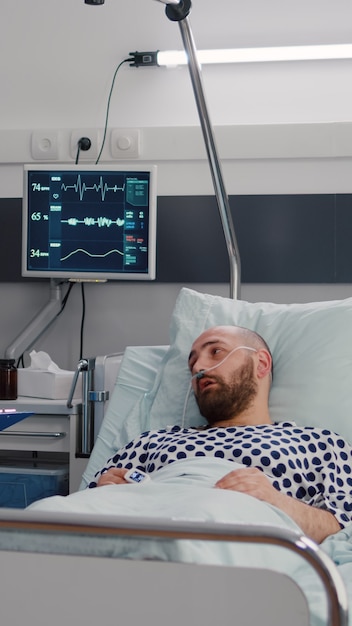 Medical nurse discussing illness treatment with hospitalized sick man resting in bed during rehabilitation therapy in hospital ward