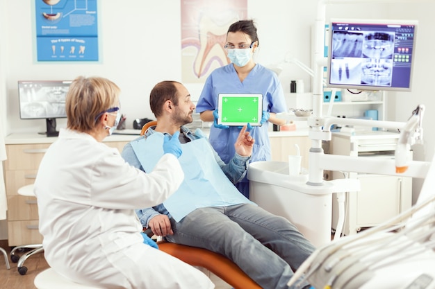 Medical nurse holding mock up green screen chroma key tablet with isolated display during somatology consultation