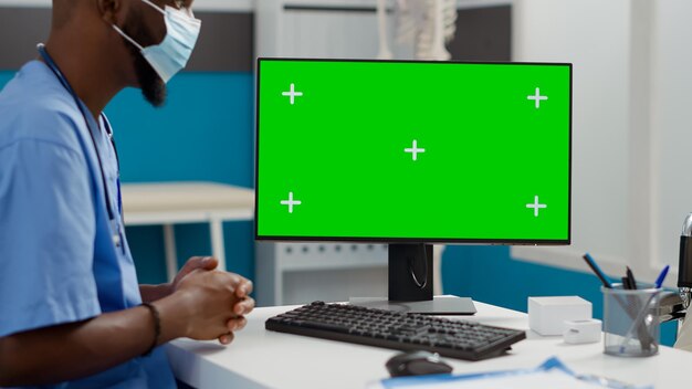 Medical nurse and woman with impairment using greenscreen on computer in cabinet. Specialist looking at blank chromakey template with isolated mockup display, patient with face mask in wheelchair.