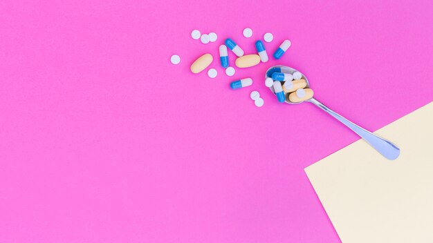 Medical pills on spoon against pink background