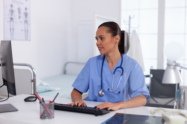 병원 사무실에서 컴퓨터를 사용하는 의사. 모니터, 약, 직업, 스크럽을 보고 있는 현대 클리닉에서 컴퓨터를 사용하는 의료 의사.
