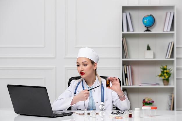 Medico abbastanza carino medico in camice bianco e cappello con il computer con la penna e le pillole