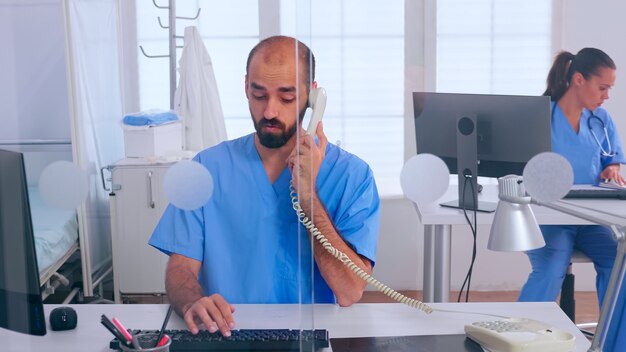 Medical receptionists working in hospital clinic answering at phone, writing on computer, making appointments. Physician in uniform writing list of consulted, diagnosed patients, making research.