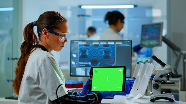 応用科学研究所でグリーンスクリーンのモックアップテンプレートを備えたタブレットに取り組んでいる医学研究者。バックグラウンドで実験を行い、ハイテクを使用してワクチンの進化を調べるエンジニア