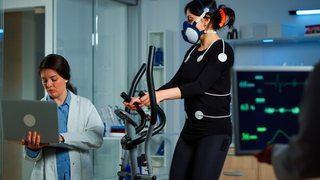신체 센서, 전극 및 심장 박동 측정 마스크를 사용하여 스포츠맨 지구력을 측정하면서 노트북을 사용하는 의료 연구원