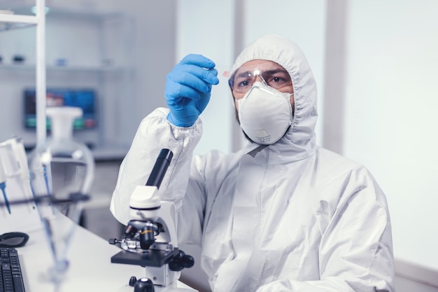 Medical scientist holding a microscope glass slide dressed in ppe during covid19. Examining vaccine evolution using high tech for researching treatment against covid19 virus.