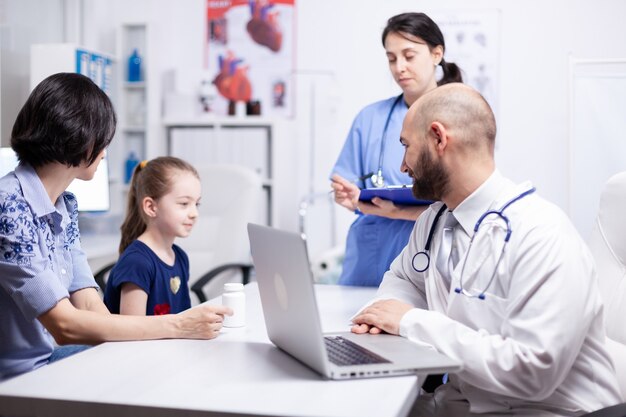 Medical staff examining sick child sittinge next to mother in hospital office. Healthcare physician specialist in medicine providing health care services treatment examination.