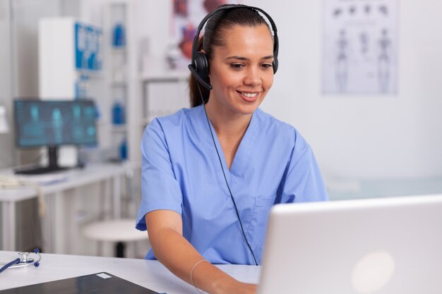 Medical staff talking with patient about prescription wearing headset with microphone in hospital office. Health care physician sitting at desk using computer in modern clinic looking at monitor.