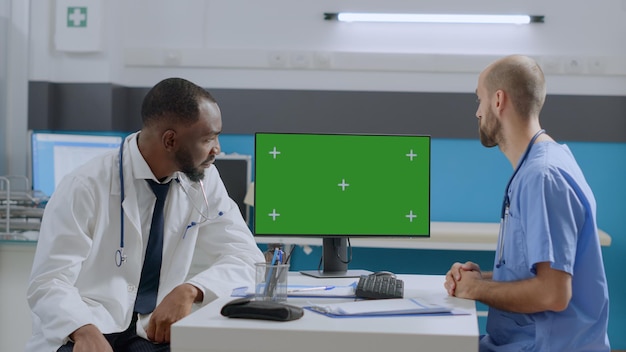 Medical team analyzing sickness diagnostic report working at healthcare treatment in hospital office. Mock up green screen chroma key computer with isolated display standing on desk. Medicine concept